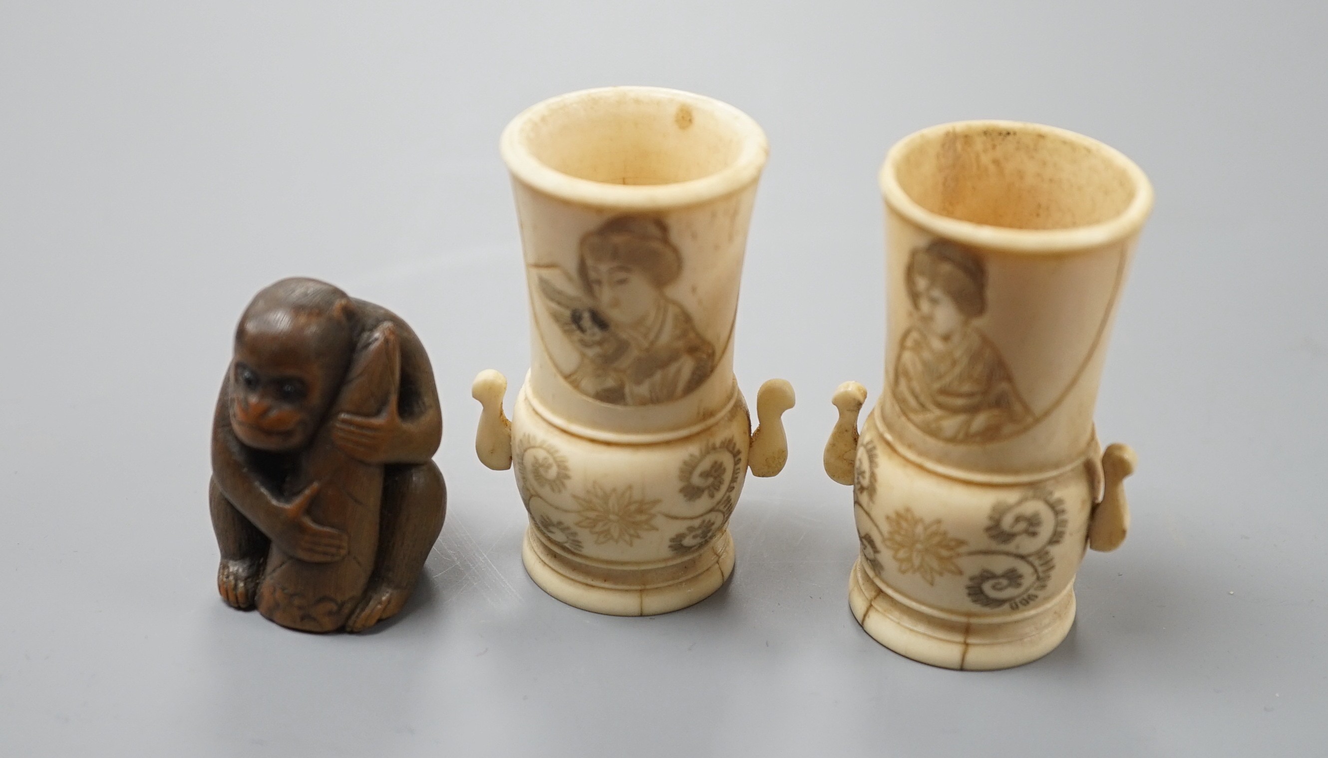 A pair of early 20th century Japanese miniature ivory vases, 5.3 cm, engraved with a lady and a wood netsuke in the form of a monkey holding a bamboo shoot (3)